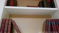 Shelf filled with multiple vintage hardcover books in dark and reddish bindings