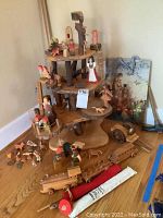 Wide view showing the wooden display stand with multi-level circular tiers holding wooden figurines and animals, wooden car and train on the floor around the display, rolled canvas bag in front, and vintage map artwork behind.