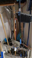 Photo of plastic corner rack loaded with rakes, brooms, brushes, and other yard tools showing overall contents.