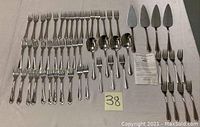 Full set showing multiple forks, spoons, and servers laid out on a white cloth.