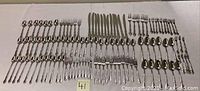 Full layout of all flatware items arranged in rows showing forks, knives, and spoons with ornate handle design.