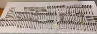 Top-down view of an assortment of forks, knives, and spoons neatly arranged on a white cloth.