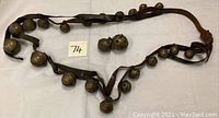Full view of the sleigh bells attached to leather straps spread out on a white surface with lot number card visible.