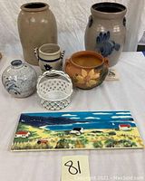 Overview photo showing six items: two large stoneware crocks, white ceramic jar and basket, Roseville vase with floral design, and a ceramic tile with a beach scene.