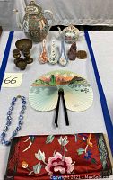 Wide view of lot including teapots, spoons, fan, brass holder, soapstone figures, embroidered textile, and necklace.