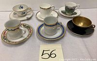 Full set of six demitasse cups and matching saucers with diverse patterns and gold accents shown on white tablecloth.