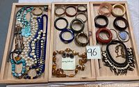 Wide view of jewelry collection laid out in wooden trays showing necklaces, bangles, and earrings.