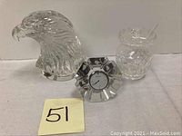 Three crystal items on a white surface: eagle head sculpture, crystal desk clock with Orrefors branding, and sugar jar with ladle.