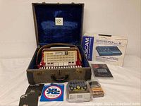Accordion in open case at center flanked by Tascam box and accessories in front