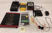 Full view of all electronics and accessories including cassette recorders, CD Walkman, self-defense audio tapes, earphones, and book.