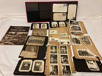 Overview of multiple black and white photographs, newspaper clippings, some mounted on cardboard and photo board, including a history book and envelopes.