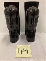 Pair of dark ebony wood carved male and female ethnic faces shaped as bookends placed side by side on white surface.