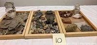 Overview of three wooden trays containing mineral rocks and a small glass jar with mineral samples.