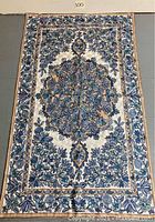 Full view of the needlework throw blanket showing entire blue floral design on white fabric with beige borders.