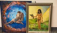 Photo shows two oil paintings side by side: a nude couple in a colorful circular pattern and a framed painting of a nude woman with ankh and bird in front of pyramids.