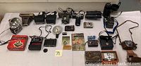 Full overview of vintage camera lot showing multiple cameras, flash units, film packs, and cases on a white surface.