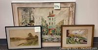 Three framed watercolor paintings shown together, including large city street scene with water stains on matting and two smaller paintings of landscape and building