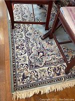 Corner close-up showing detailed floral and geometric pattern in cream, purple, and blue colors with fringed edges.