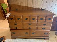 Front view of wooden dresser showing four rows of drawers with black ornate handles.
