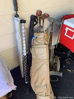 Vintage golf bag with wooden and metal golf clubs, golf umbrella, and golf ball container.