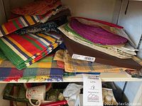 Shelf with folded assorted cloth placemats and napkins showing multicolor striped, plaid, and bright textures.