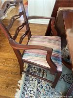 Armchair showing carved wooden arms, ladder back and striped fabric seat.