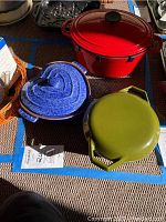 Three Dutch ovens: red oval cast iron, blue heart-shaped ceramic, olive green round cast iron with lid.