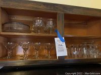 Wide shot of kitchen cabinet shelf showing rows of champagne glasses on bottom shelf, glass bowl, and shrimp cocktail servers on top shelf.