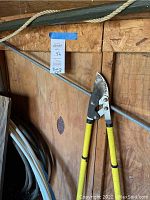 Photo showing yellow-handled loppers hanging on a wooden wall with a tag marked 92