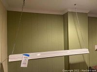 Photo of the entire overhead grow light fixture hanging by chains from the ceiling in a basement with green panel walls.