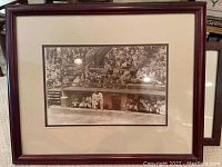 Framed black and white photo of Jackie Robinson sitting in the dugout at Ebbets Field with crowd in background.