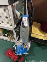 Kenmore Elite upright vacuum cleaner in silver/gray color alongside vacuum bags and a red handheld vacuum on the floor near storage shelves.