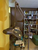 Side view showing the lamp mounted on an adjustable arm with magnifying glass and light head, metal construction with matte gray finish.