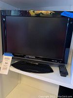 Front view of Sharp HD TV with built-in DVD player, base stand, power indicator light, and remote control.