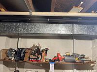 Shelf with various tools including boxed items, power tools, hand tools, and accessories spread across the surface.