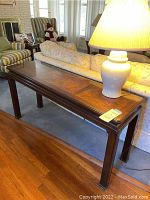Sofa table shown behind the couch in a living room setting with lamp on top, highlighting the wood grain and inlaid tabletop design.