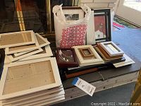 Variety of picture frames stacked on table with some 8x10 white frames and assorted smaller frames in different colors.