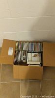Photo showing a cardboard box containing multiple CDs, some stacked and some aligned upright.