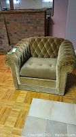 Front view of olive green crushed velvet armchair with tufted diamond pattern on back and sides, square seat cushion, and rolled arms.