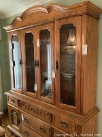 Frontal view of the oak china cabinet showing carved details, glass doors, brass handles, and interior lighting reflecting in upper display area.