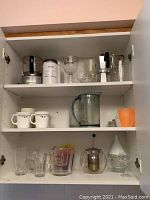 Glassware, mugs, measuring cups, espresso stove top, coffee grinder, and tea infuser displayed on kitchen shelves.