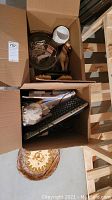 Top view of two cardboard boxes containing a computer keyboard, wooden horse figurine, glass bowls, white ceramic vase, decorative sun plate, a wooden massage tool, and cords.
