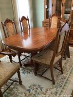 Full view of the oak dining table and six chairs arranged on a floral rug.