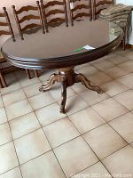 Full view of the oval dining table with mahogany finish, glass top, and inlaid pedestal base, showing the overall shape and condition.