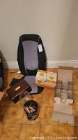 Overview of the entire lot showing the chair back massager, wooden jewelry box, wood puzzle games in a clear container, and one visible box of Arcoroc glasses.