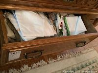 Open drawer showing folded white and patterned kitchen and table linens inside wooden drawer.