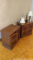Two wooden side tables placed side by side against a wall, showing the stained wood surface, mismatched metal pulls, and traditional boxed design.