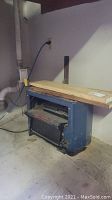 Front left angle showing planer under wood stock on table.