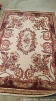 Full view of the cream-colored floral area rug with a burgundy border, showing the full design.
