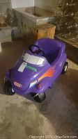Front-left angled view of the purple Little Tikes ride-on toy car showing flame decal and steering wheel.